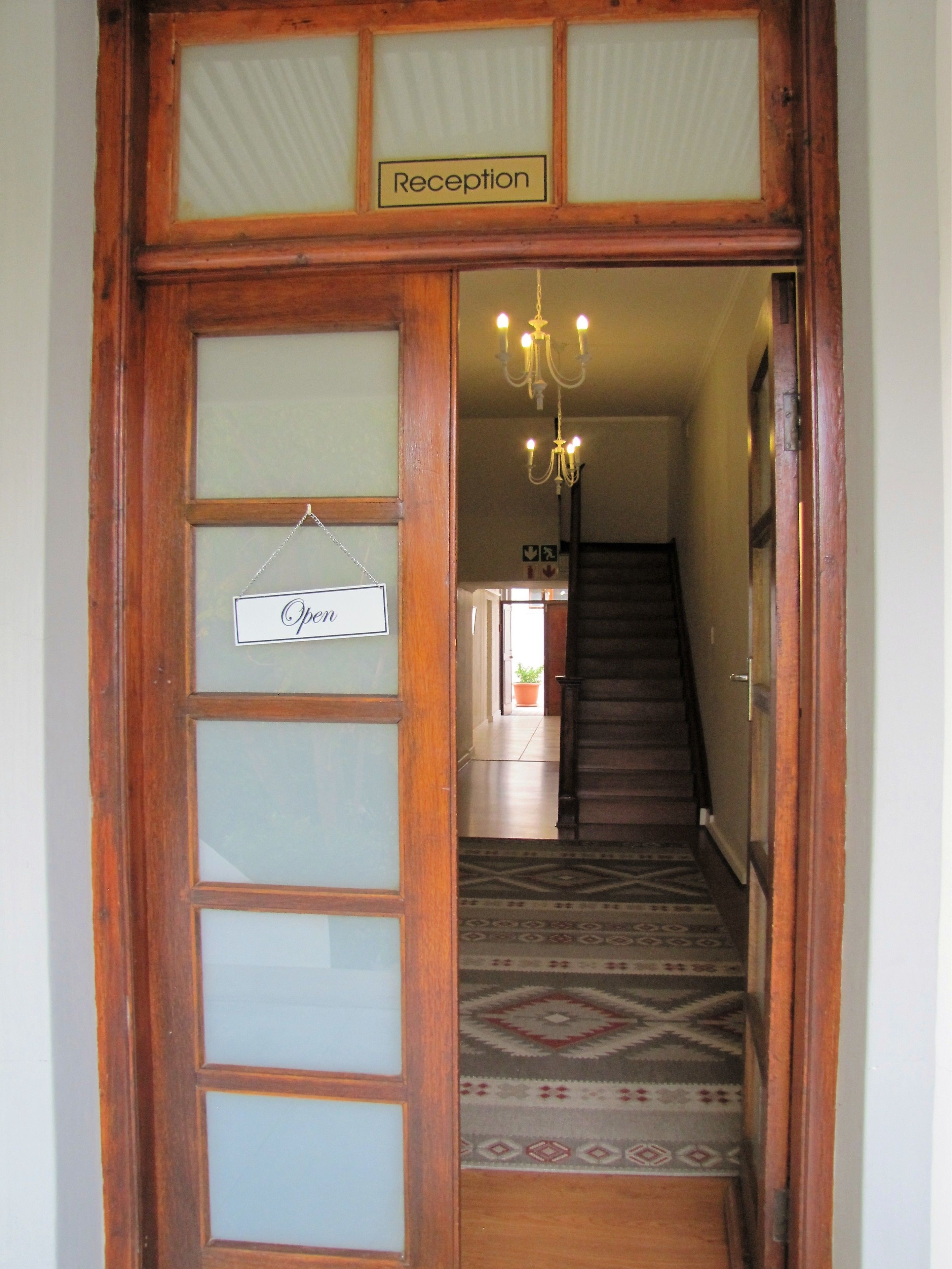 Un área de recepción con una puerta de madera, una araña de cristal y una alfombra estampada.