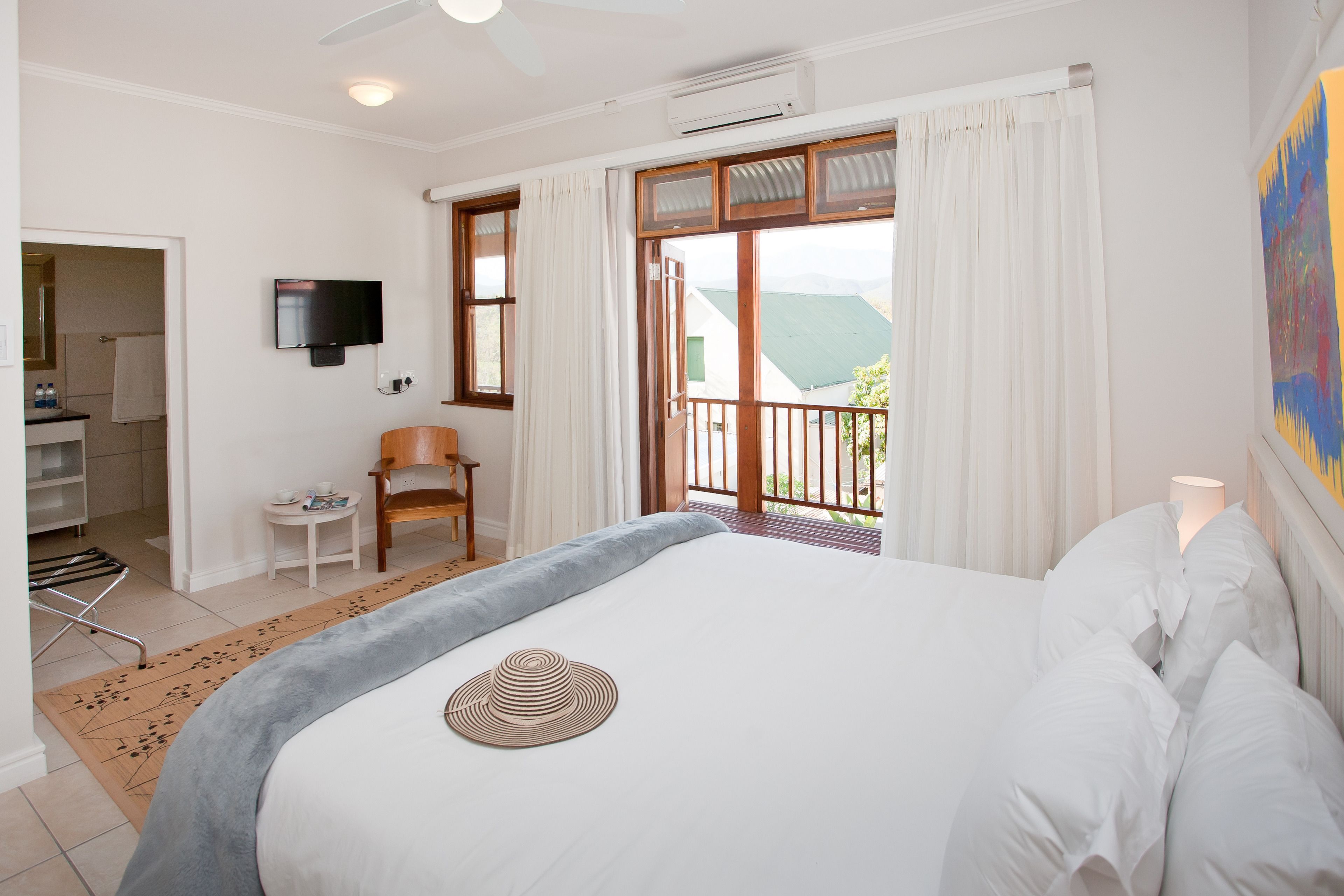 Ein Hotelzimmer mit Bett, einem an der Wand befestigten Fernseher, einem kleinen Tisch mit Stuhl und einem Balkon mit Blick.