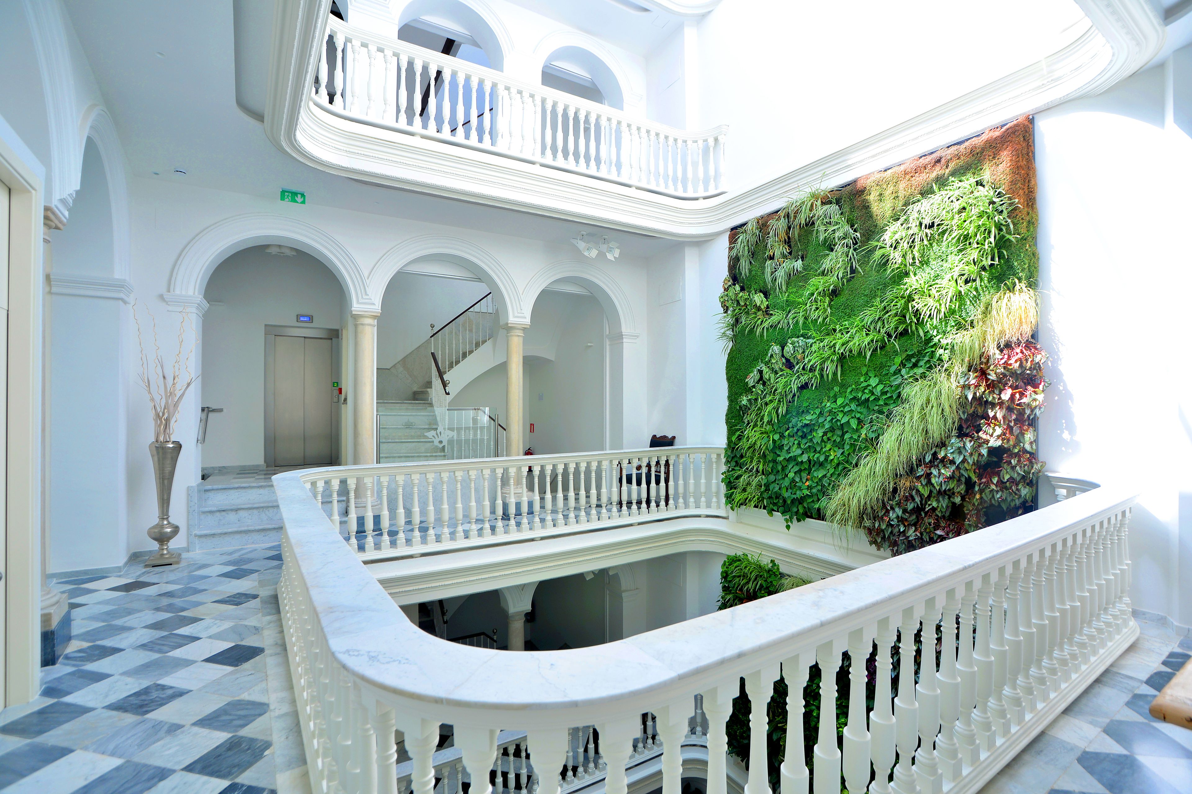 A multi-level interior with a checkered floor, white balustrades, and a green vertical garden wall.