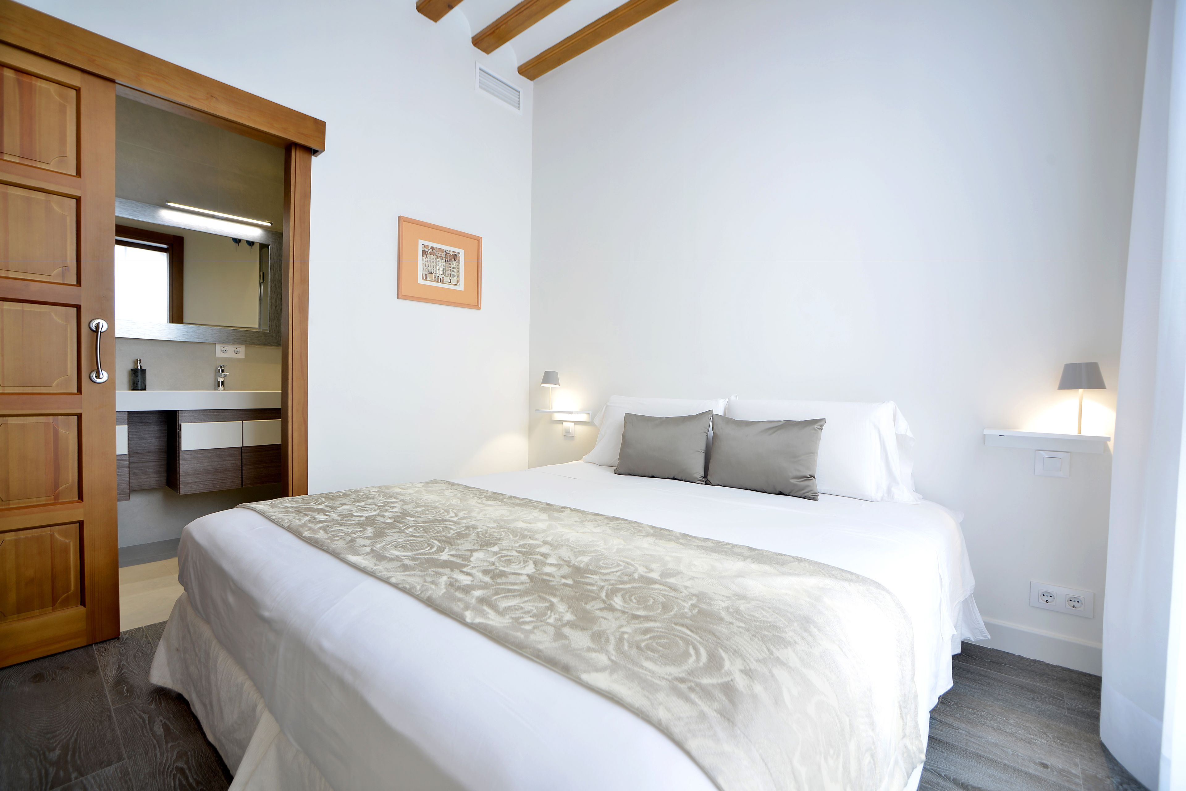 A bedroom with a bed, wooden wardrobe, and a bathroom visible through an open door.