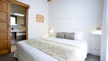 A bedroom with a bed, wooden wardrobe, and a bathroom visible through an open door.