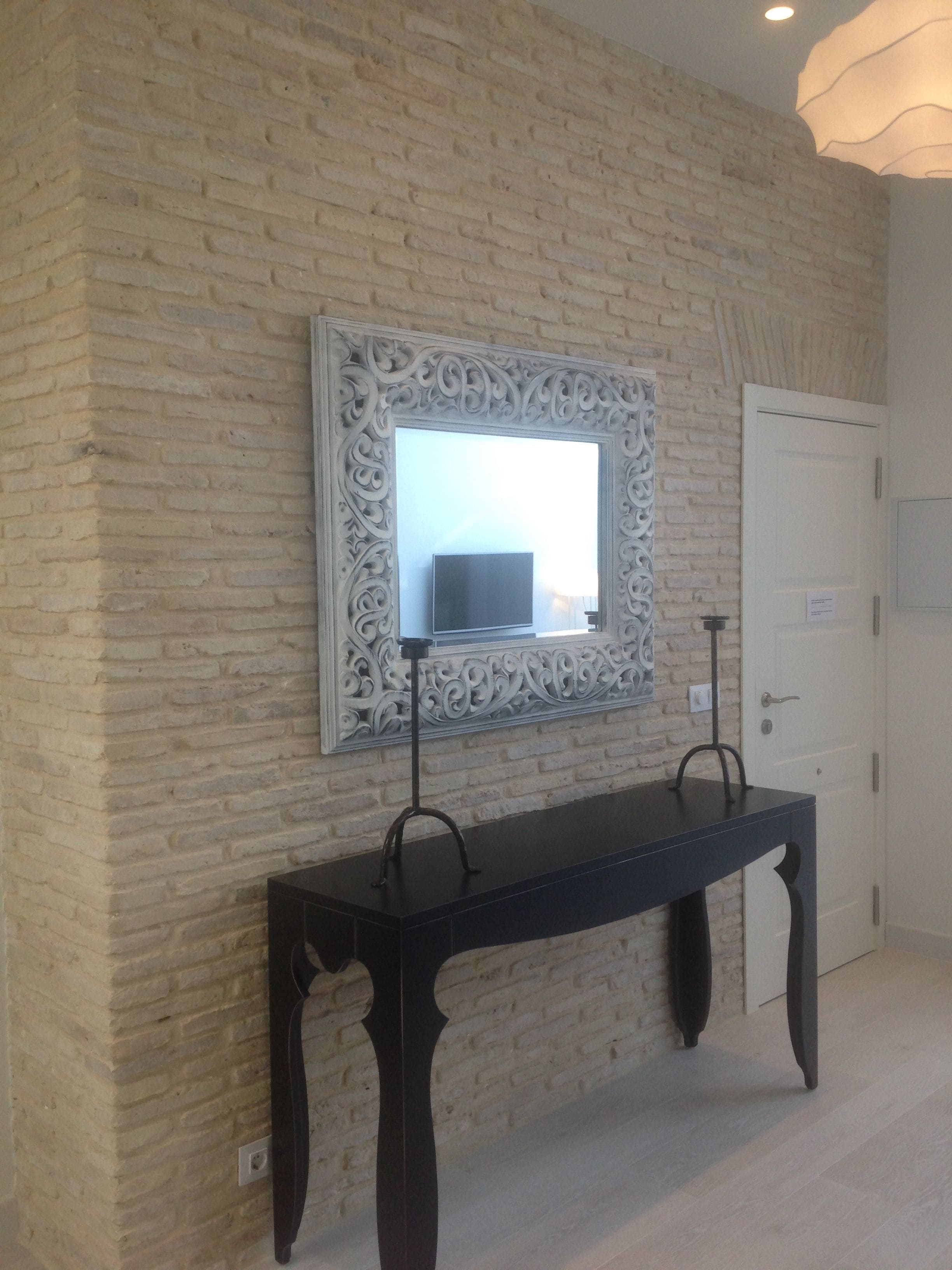 A room with a brick wall, a decorative mirror, a black console table, and a white door.