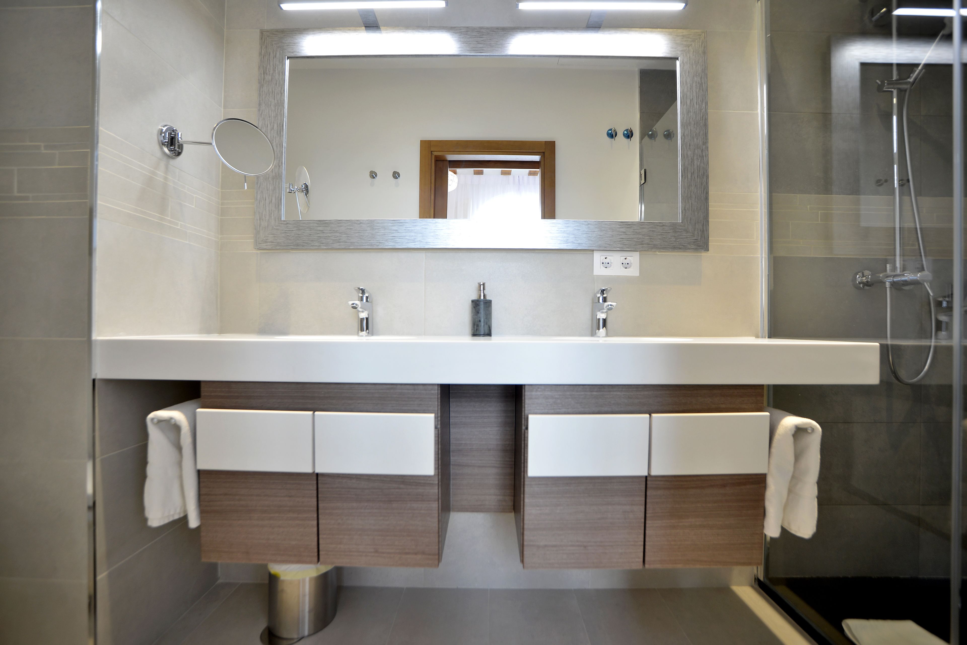 Ein modernes Badezimmer mit einem großen Spiegel, zwei Waschbecken und einer Dusche.
