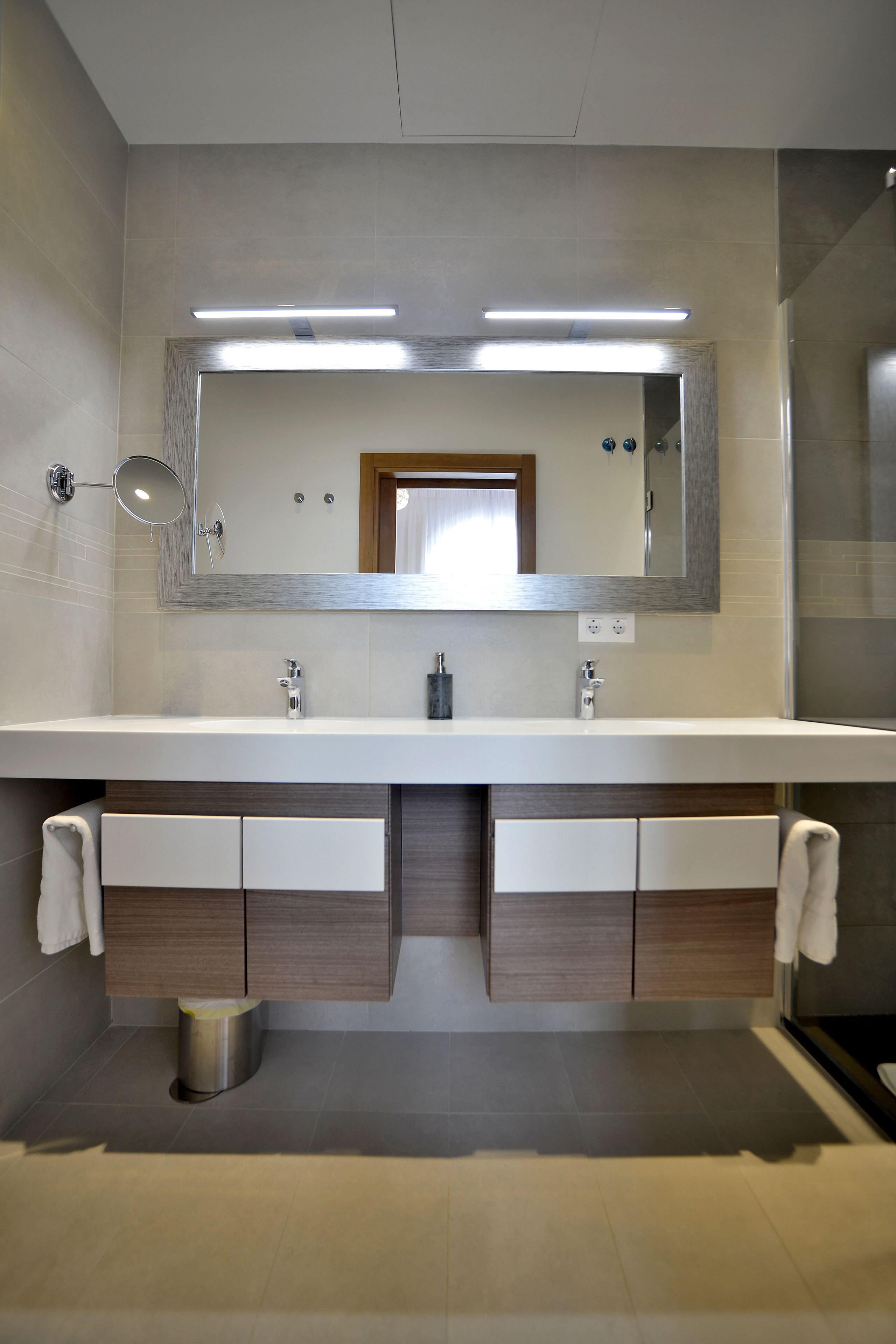 Un baño moderno con lavamanos doble, dos espejos y zona de ducha.