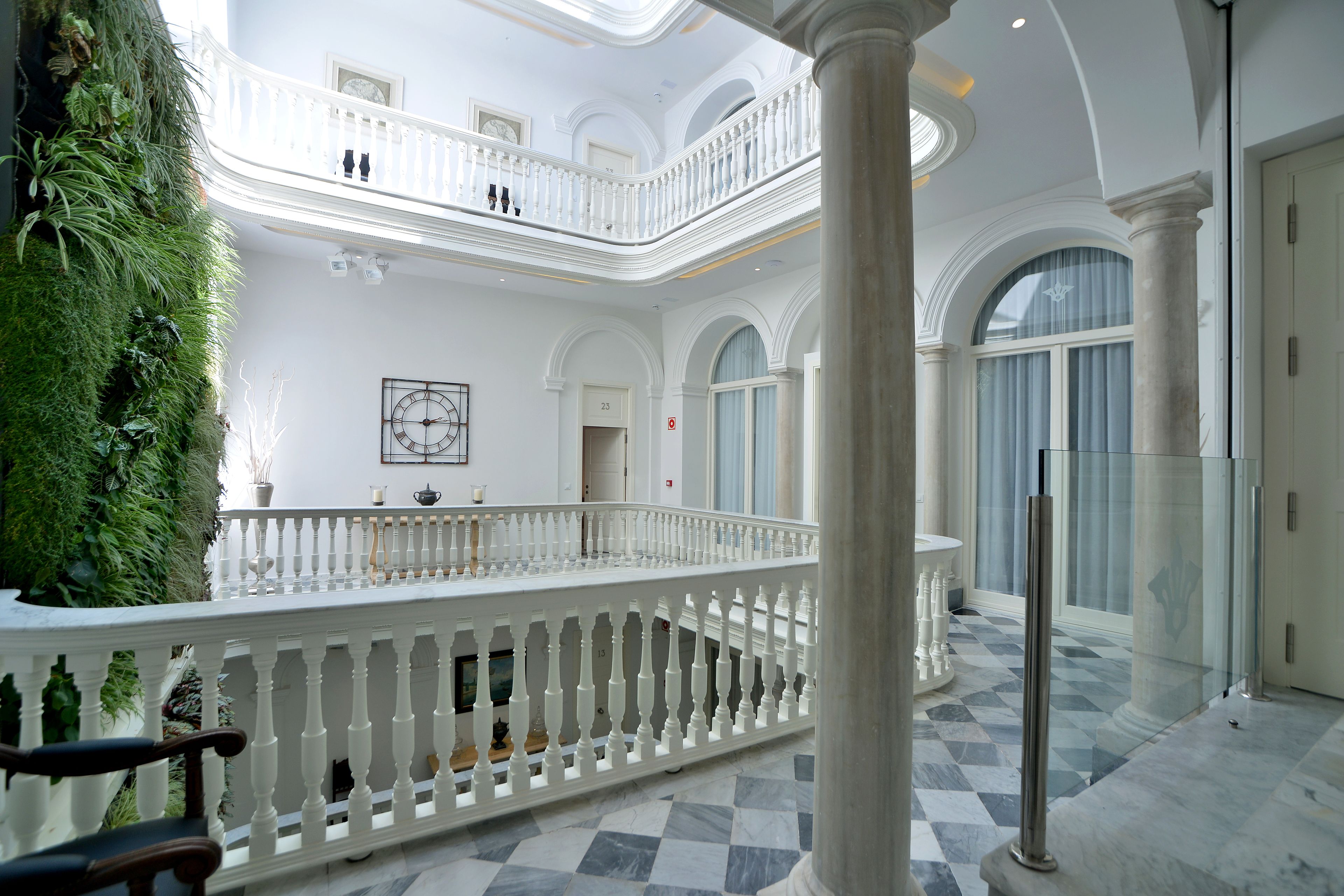 A grand interior with a white balustrade, a green vertical garden, and a checkered marble floor.