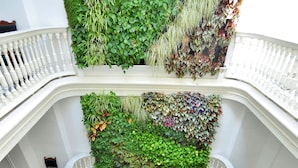 Un atrio de varios niveles con suelo a cuadros, balaustradas blancas y diversas plantas en las paredes.