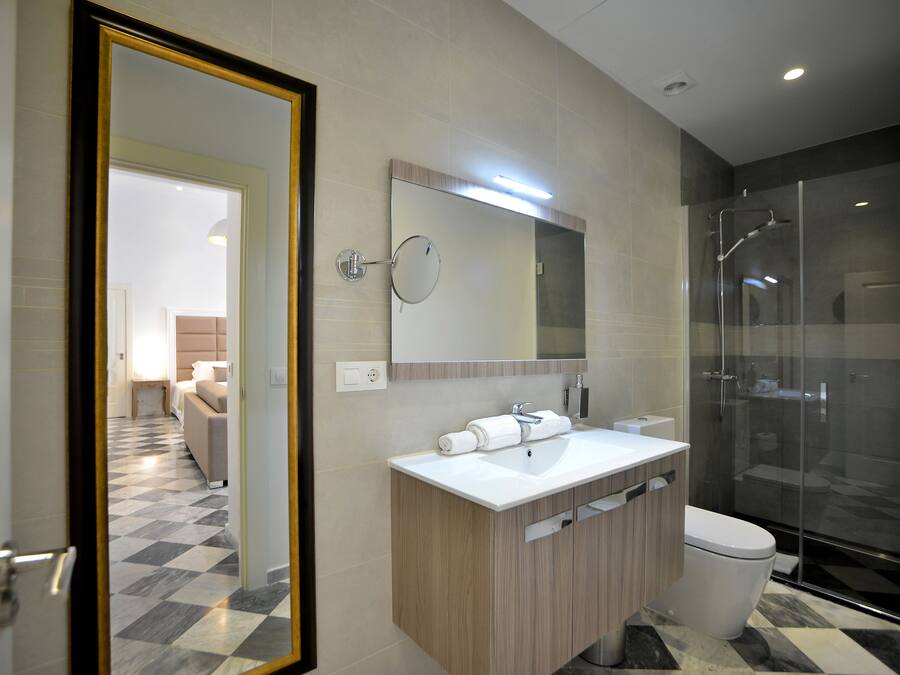 Un baño moderno con un espejo grande, un lavabo, un inodoro y una ducha con mampara de vidrio.