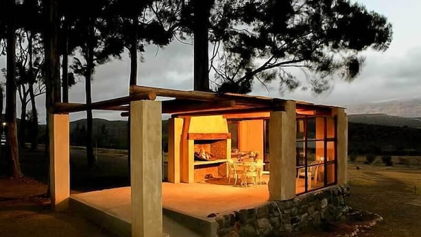 A rustic cabin with a stone foundation, a wooden porch, and a visible fireplace. - Keurfontein Country House (Willowmore)