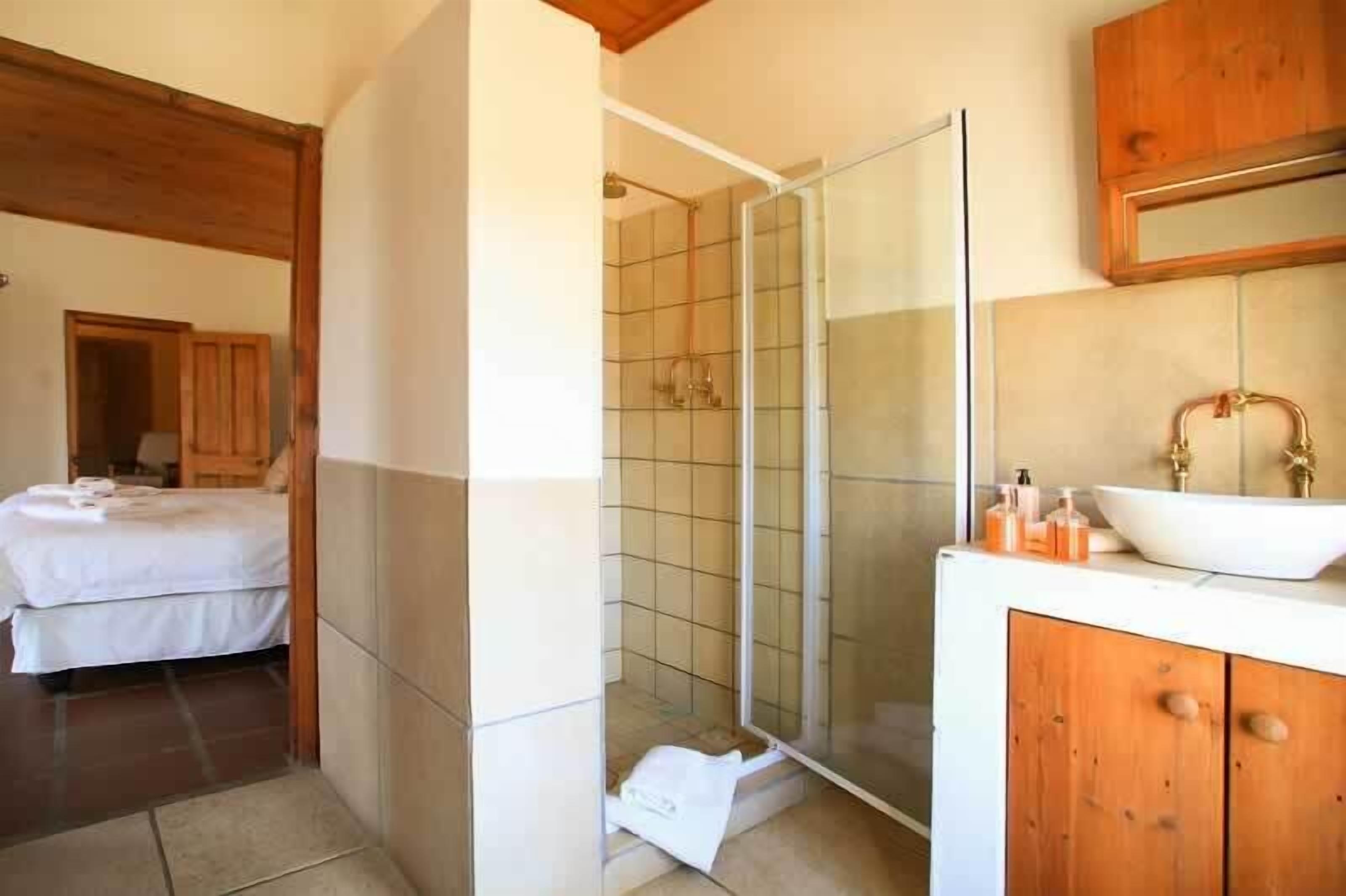 Un bagno con box doccia in vetro, un lavandino bianco con lavabo a incasso e mobili contenitori in legno.