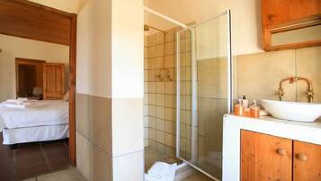 Un bagno con box doccia in vetro, un lavandino bianco con lavabo a incasso e mobili contenitori in legno.