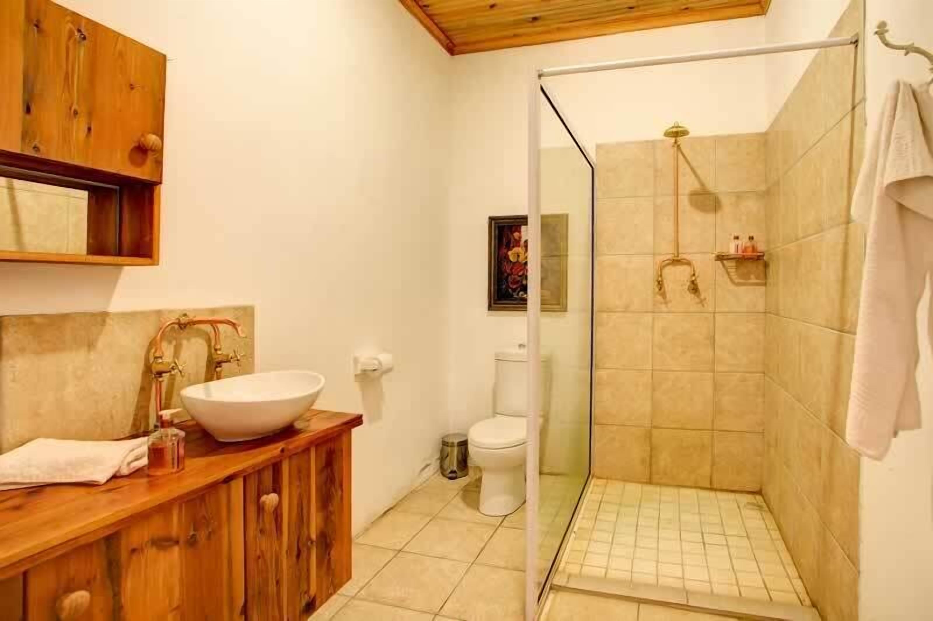 Een badkamer met een houten wastafelmeubel, een witte wasbak, een douchecabine van glas en een toilet.