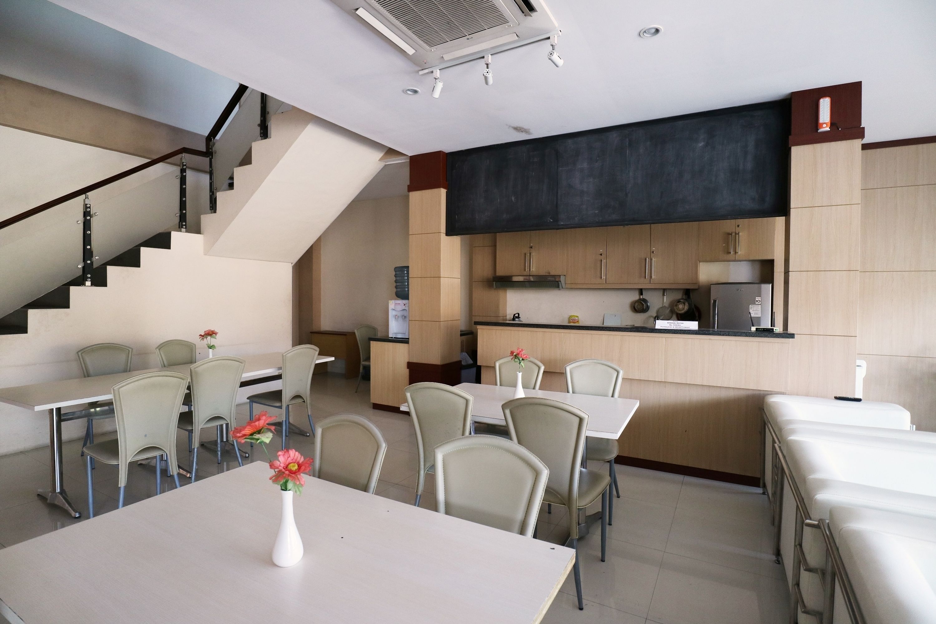 A modern hotel dining area with a staircase, a kitchen area, and several dining tables with chairs.