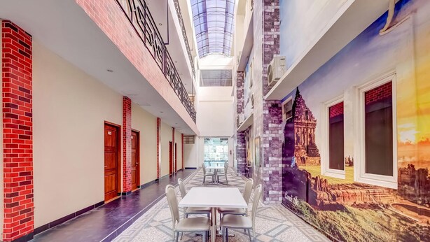 A corridor with a central table and chairs, a high ceiling with a skylight, and a mural on the right wall. - Tembok Batu Residence (Pogung Lor)