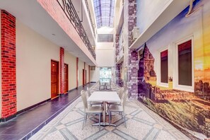 Un pasillo con una mesa y sillas centrales, un techo alto con tragaluces y un mural en la pared derecha.