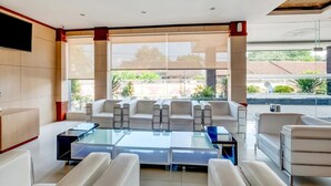A modern hotel lobby with a seating area, large windows, and a flat-screen TV on the wall. - Tembok Batu Residence (Pogung Lor)