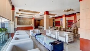 A modern hotel lobby with white sofas, a glass coffee table, and a staircase with red accents. - Tembok Batu Residence (Pogung Lor)