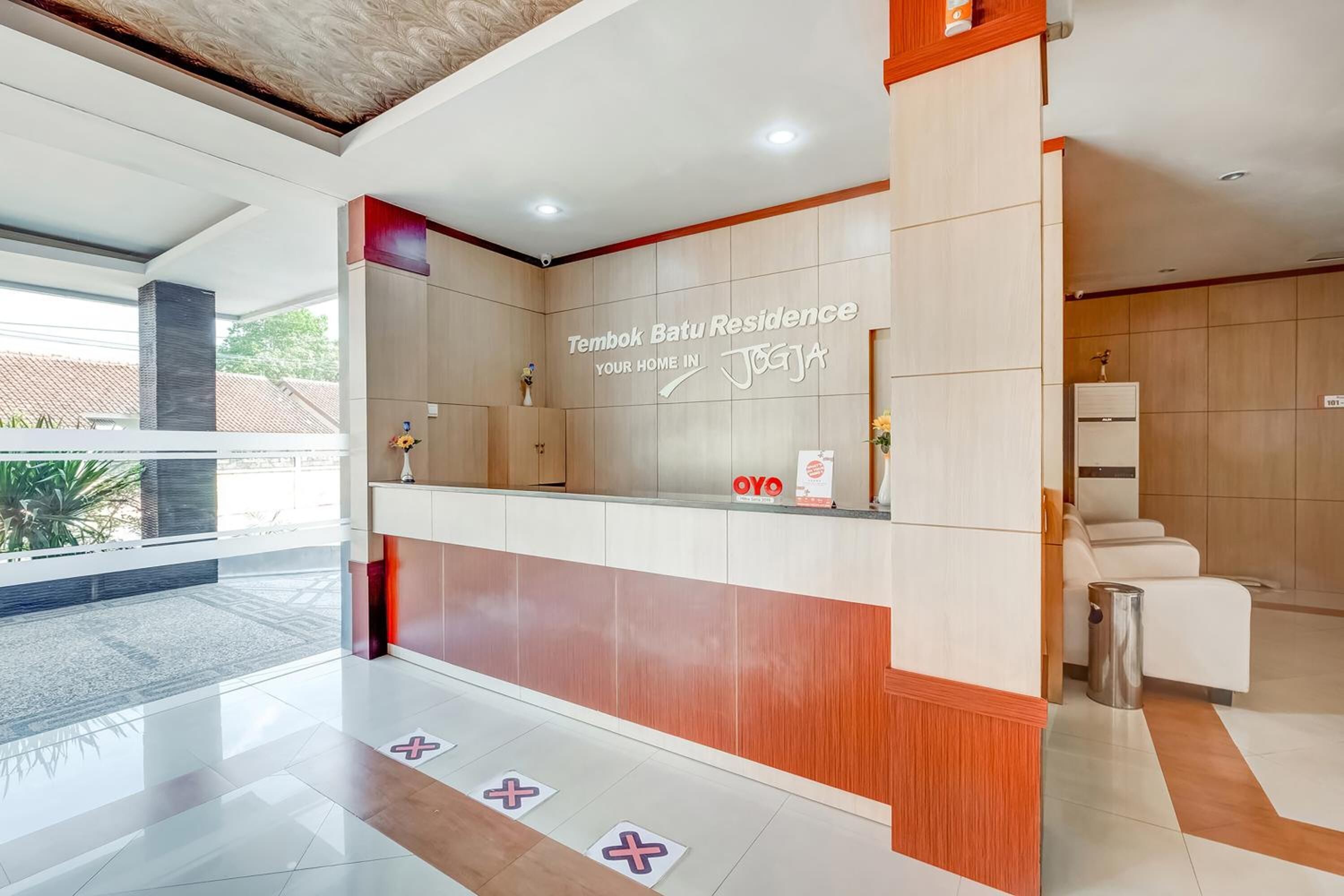 A reception area with a wooden reception desk, a sign reading "Tambok Batu Residence," and a view of the outside.