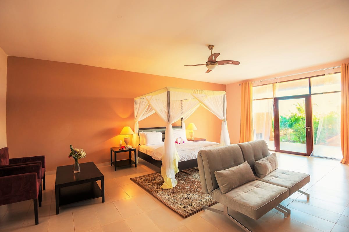 A bedroom with a four-poster bed, a sofa, a coffee table, and a nightstand with lamps.