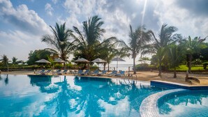 Una piscina con sillas de descanso y sombrillas, rodeada de palmeras.