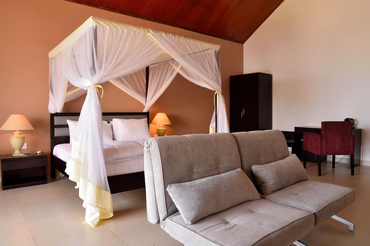 A bedroom with a four-poster bed, a sofa, bedside lamps, and a desk.