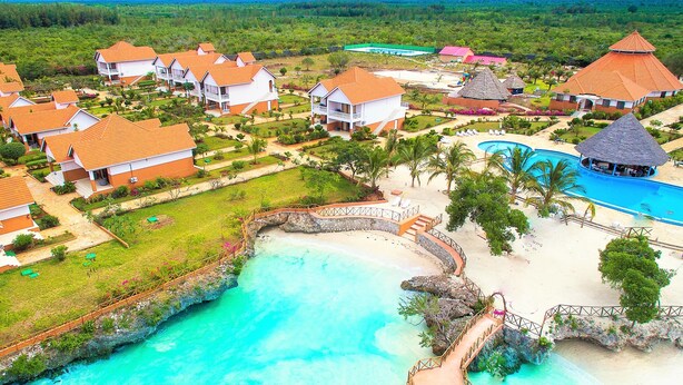 Un complejo turístico con varias construcciones tipo bungalow, una piscina central y una zona de playa.