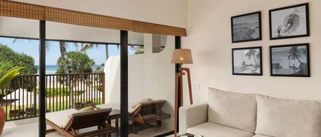 A modern living room with a sofa, a coffee table, and a view of the ocean through large glass doors. There are framed pictures on the wall and a lamp.