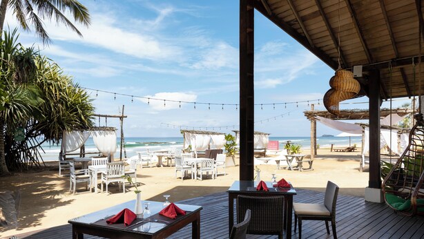 A beachside restaurant with outdoor seating, string lights, and a view of the ocean. - Ekho Surf (Bentota)