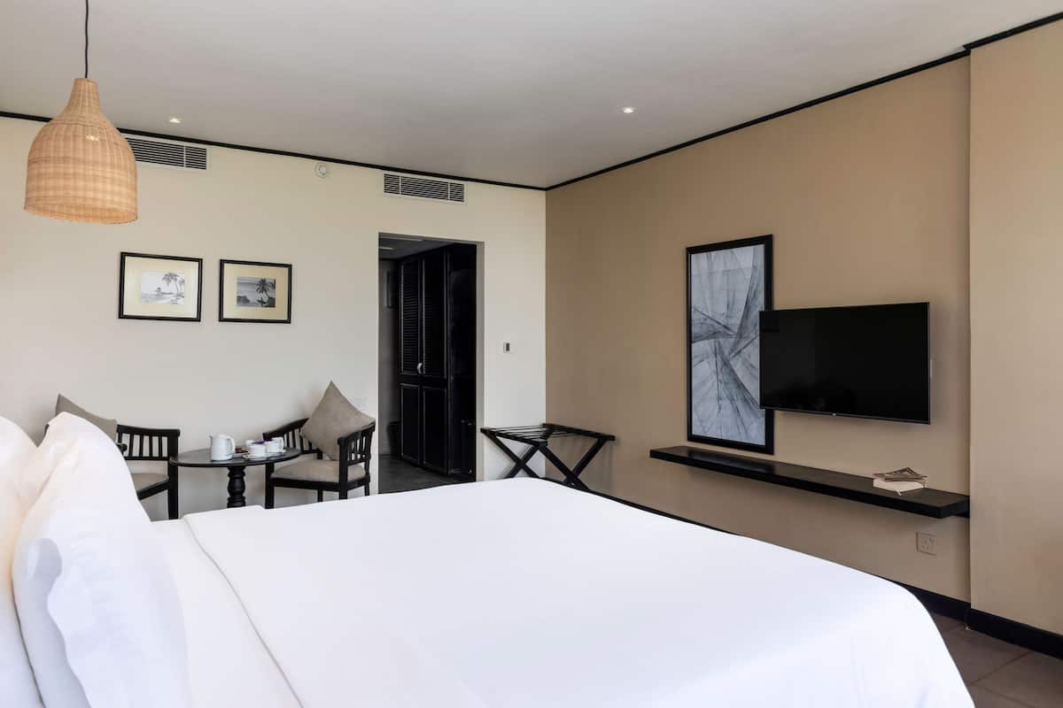 A hotel room with a bed, a TV mounted on the wall, a small table with chairs, and two framed pictures on the wall.