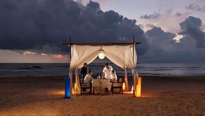 A beachside dining setup with a canopy, table, chairs, and ambient lighting. - Ekho Surf (Bentota)