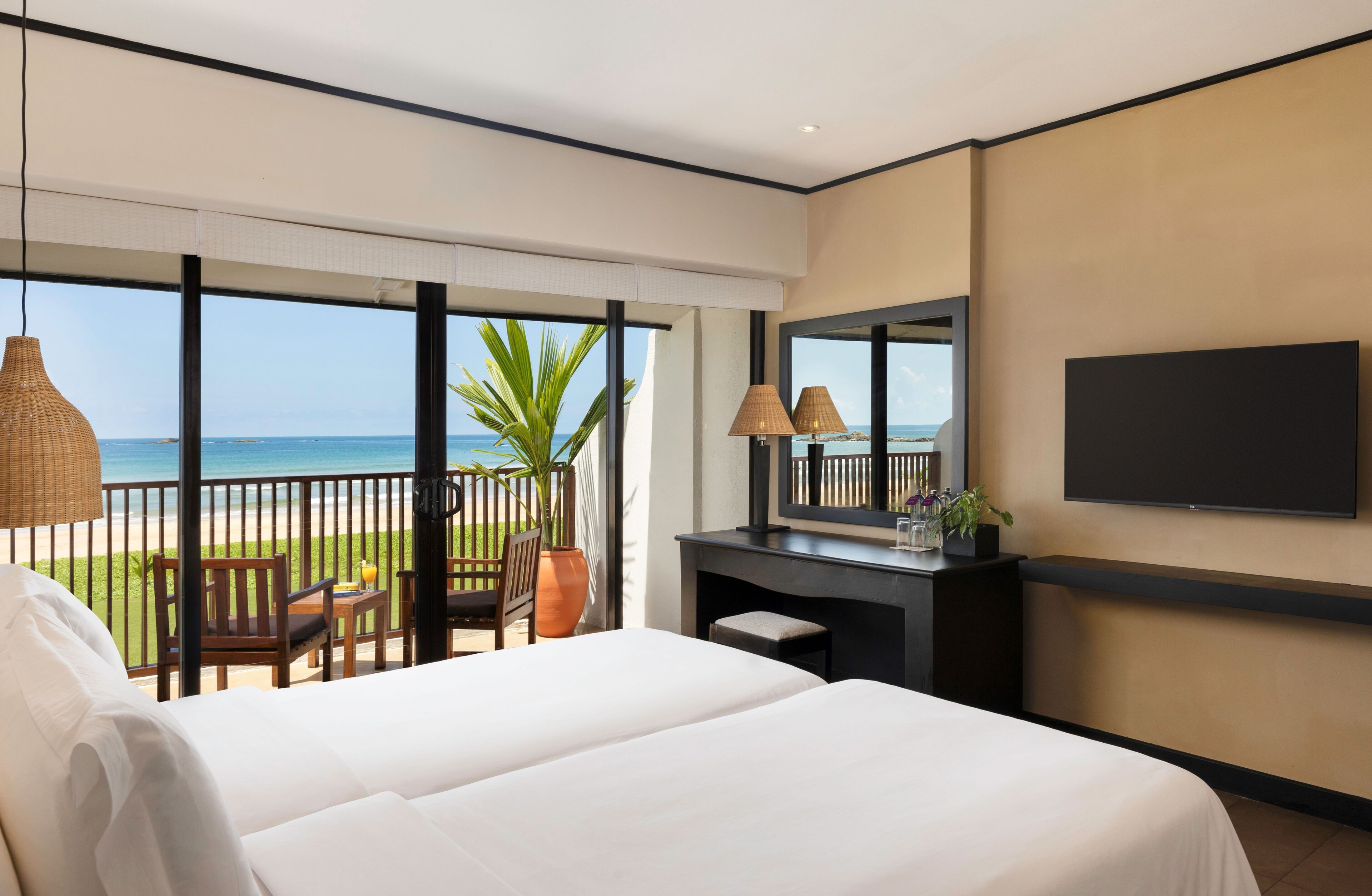A hotel room with a large bed, a desk with a TV, and a balcony with a view of the sea.