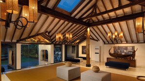 A spacious living area with high ceilings and exposed beams, featuring modern furniture and a large window overlooking a garden. - Ekho Surf (Bentota)