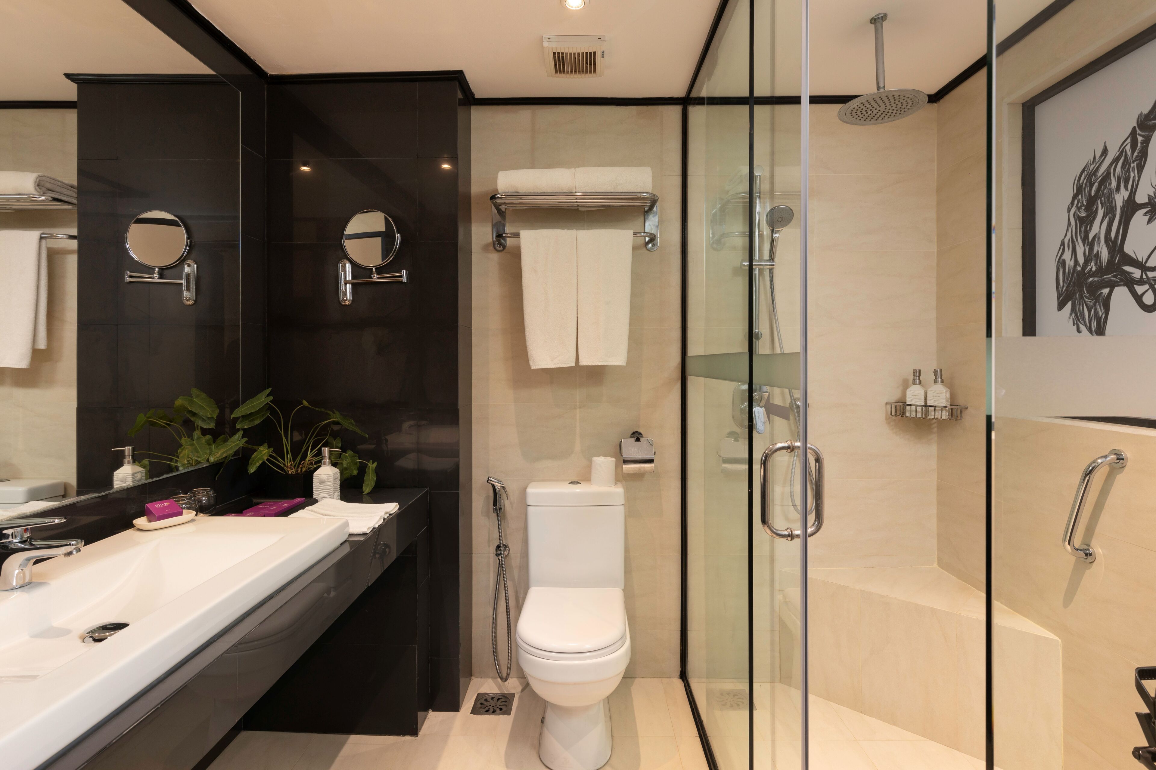 A modern bathroom with a large mirror, a white sink, a toilet, and a glass-enclosed shower area.