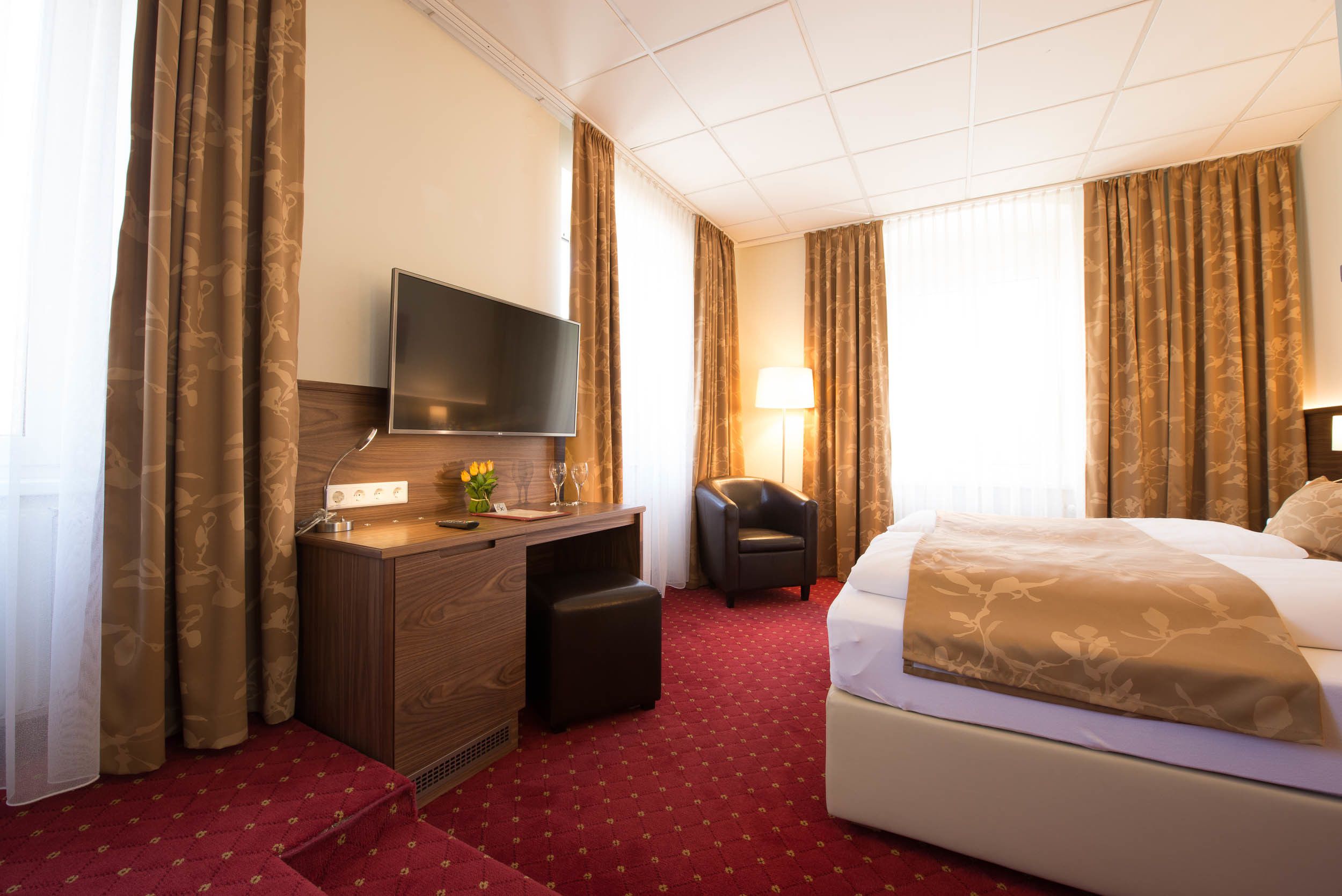 Ein Hotelzimmer mit Bett, Schreibtisch, Stuhl, Fernseher und Lampe.