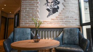 A modern interior with a brick wall, a large window, two blue armchairs, and a wooden table with a vase. - Hotel Beethoven (Hinterbruhl)