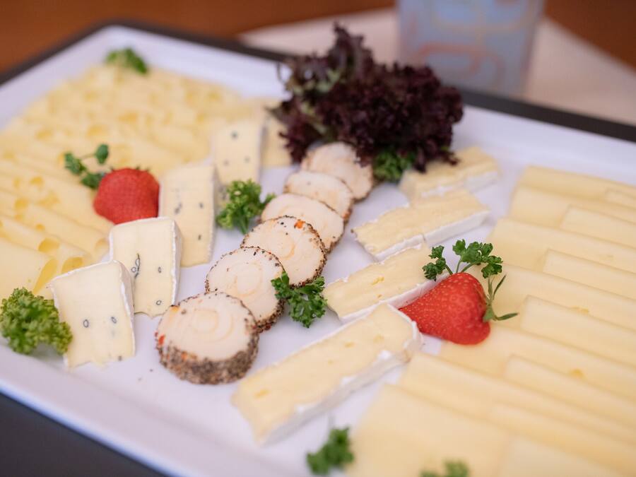 A cheese platter with various types of cheese, strawberries, and parsley on a white plate.