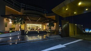 A modern hotel entrance with a covered walkway, palm trees, and a well-lit facade.