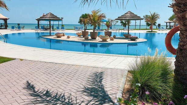 A pool area with lounge chairs and umbrellas, surrounded by palm trees and a view of the sea. - Simaisma, A Murwab Resort (Simaisma)