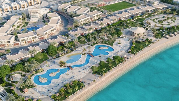 An aerial view of a resort with multiple buildings, a large swimming pool, and a beach.