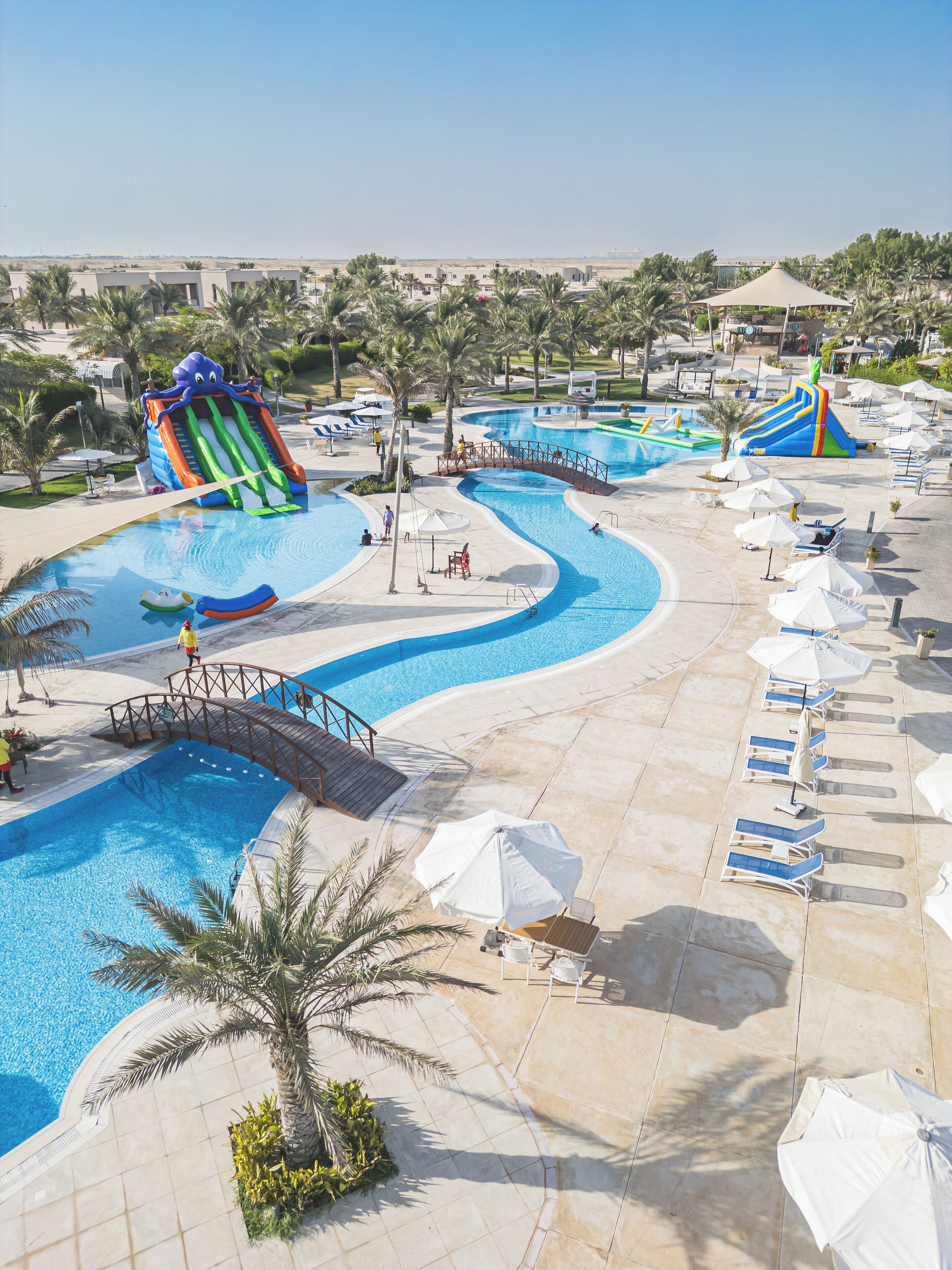 Zona de piscina en un resort con toboganes acuáticos, sillas de descanso y sombrillas.
