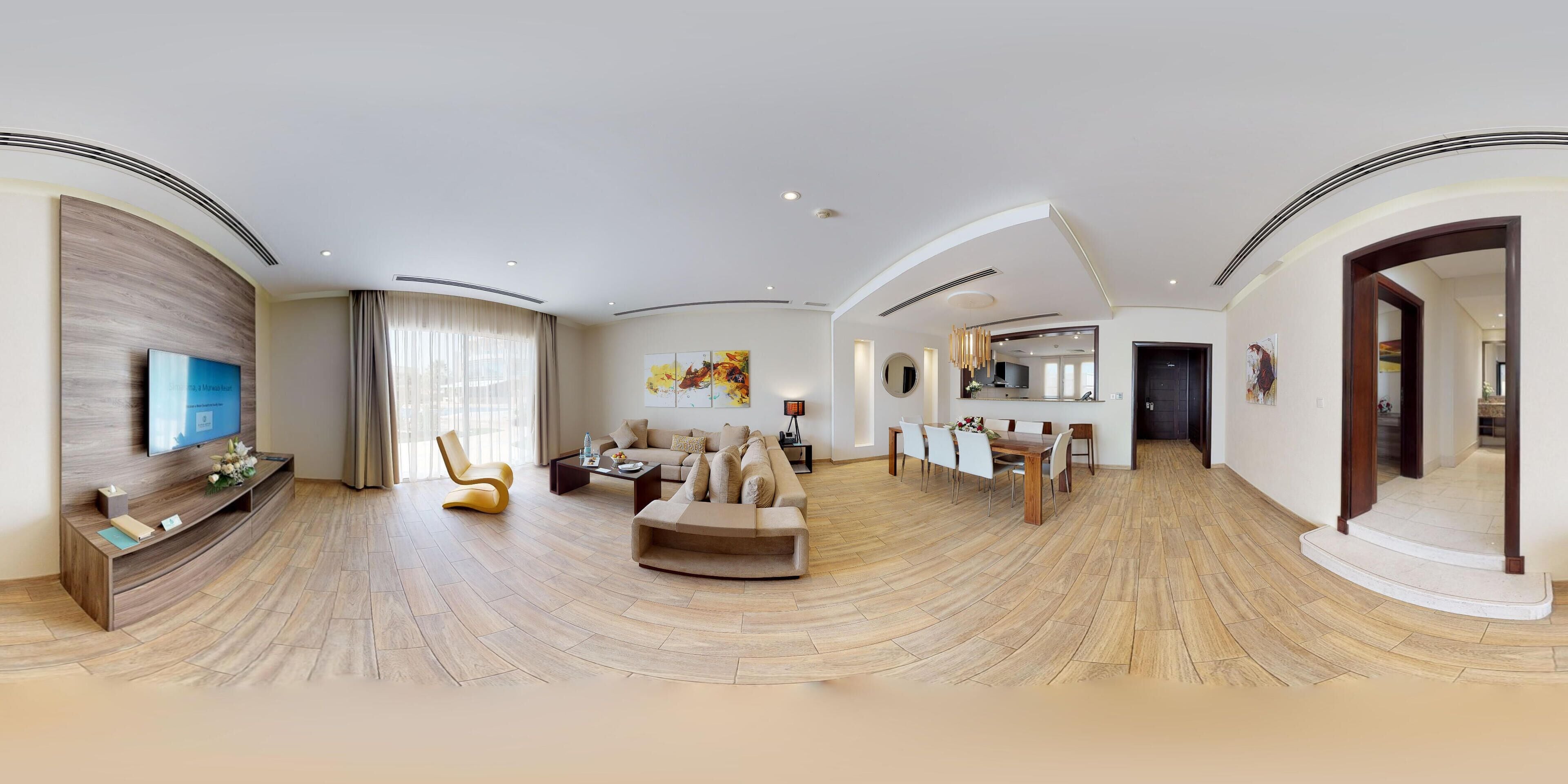 A spacious living area with a curved ceiling, a flat-screen TV mounted on the wall, a sofa, a coffee table, and a dining area with chairs and a table.