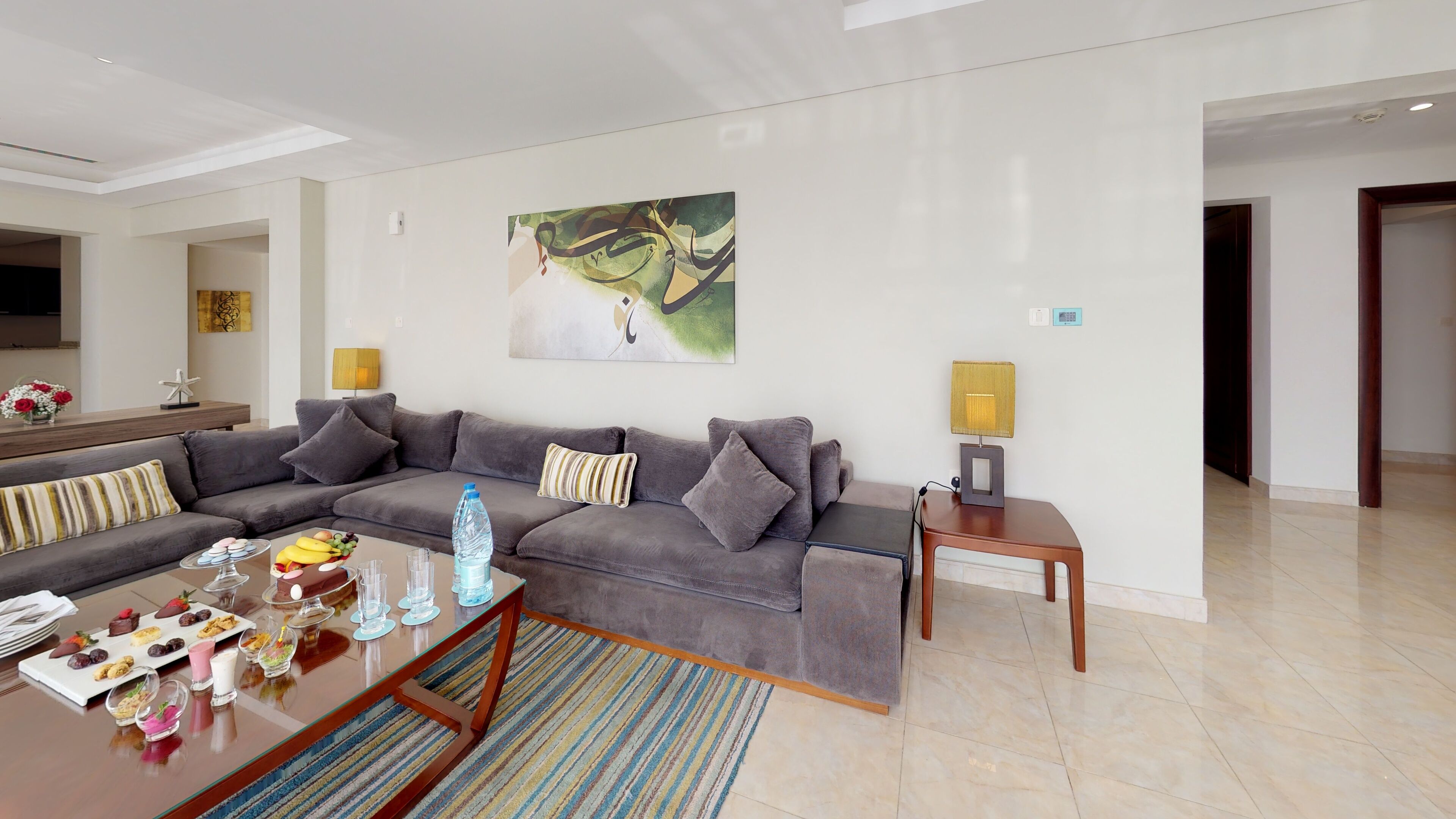 Una sala de estar moderna con un sofá gris, una mesa de centro con aperitivos, un cuadro en la pared y una lámpara sobre una mesita auxiliar.