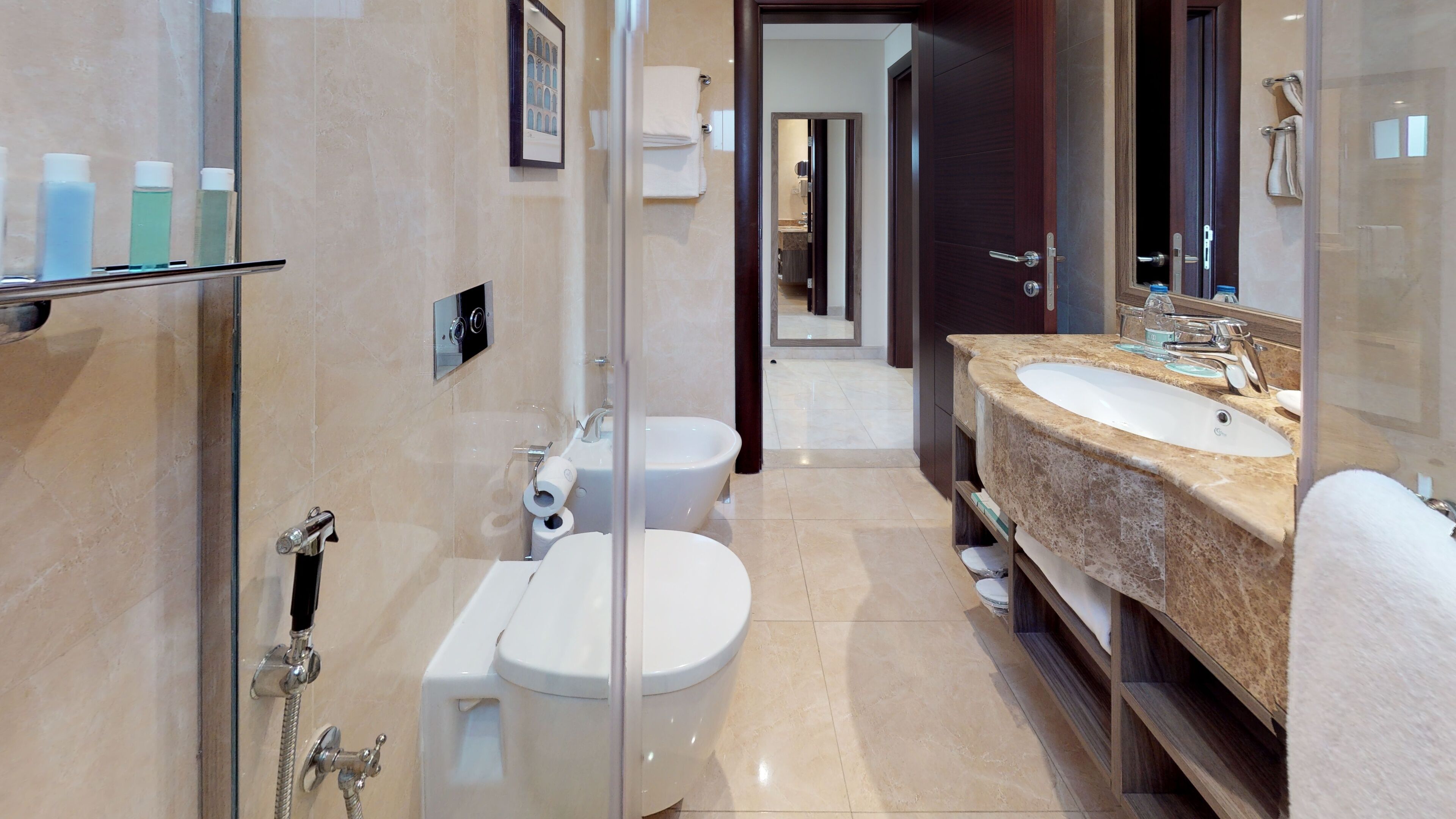 A modern bathroom with a glass shower enclosure, a toilet, a bidet, and a double sink vanity.