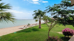 A beach view with a grassy area, a hammock, and a row of white lounge chairs. - Simaisma, A Murwab Resort (Simaisma)