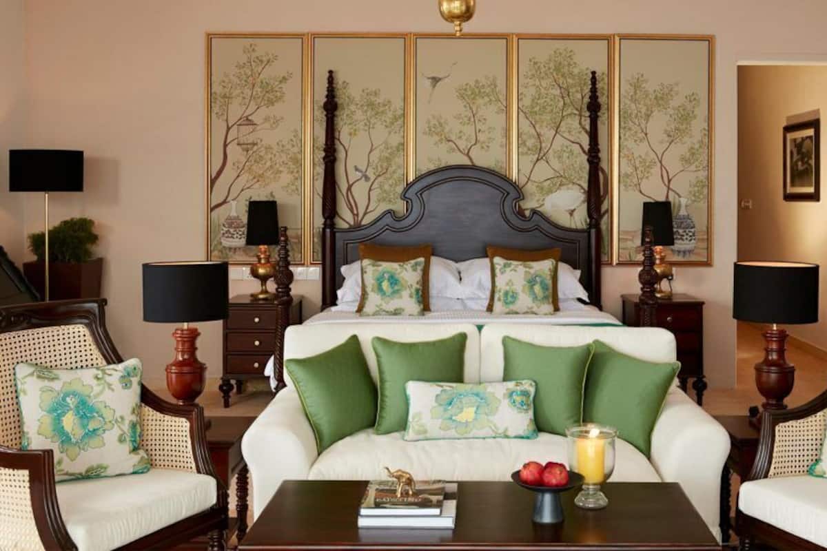 Une chambre avec un grand lit, des oreillers verts et blancs, une table de chevet avec un livre et une bougie, et un mur orné d’un tableau représentant un arbre.