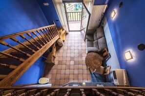 A staircase leading to a balcony with a view of a garden, a seating area with a round table, and a wall-mounted air conditioning unit.