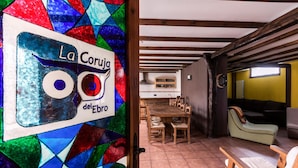 A cozy interior with a stained glass window reading "La Coruja del Ebro," a dining area with wooden furniture, and a living space with a sofa and chairs. - CTR La Coruja del Ebro (Valderredible)