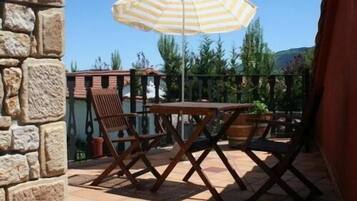 Un patio al aire libre con una mesa y sillas, un paraguas a rayas y un muro de piedra.