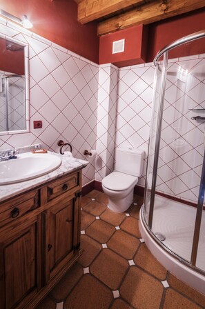 A bathroom with a wooden vanity, white tiles, a toilet, and a glass shower enclosure.
