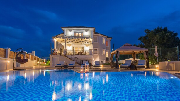 A swimming pool with a view of a two-story building with balconies and outdoor seating. - Frido Luxury Villa (Zakynthos)