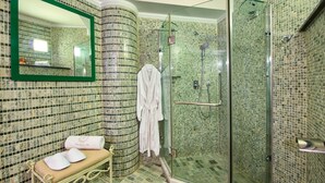 Un baño con cabina de ducha de vidrio, un banco con toallas y un espejo con marco verde.